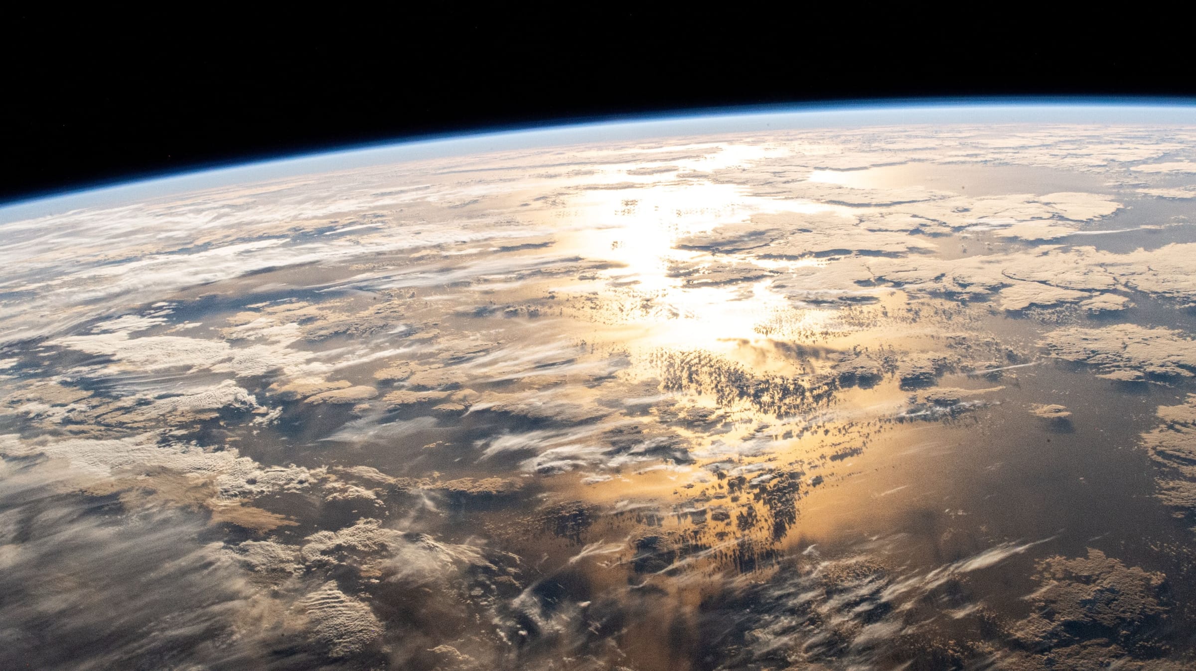 Earth's horizon from orbit, sunlight reflecting off the ocean through clouds